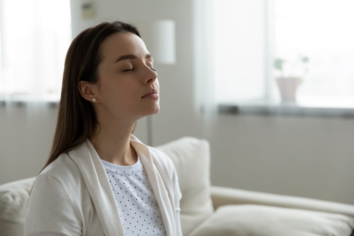 Calm serene woman resting sitting on couch in modern living room closed her eyes breath fresh humidified air. Fatigue relief repose, boost inner balance and mindfulness, meditation practice concept